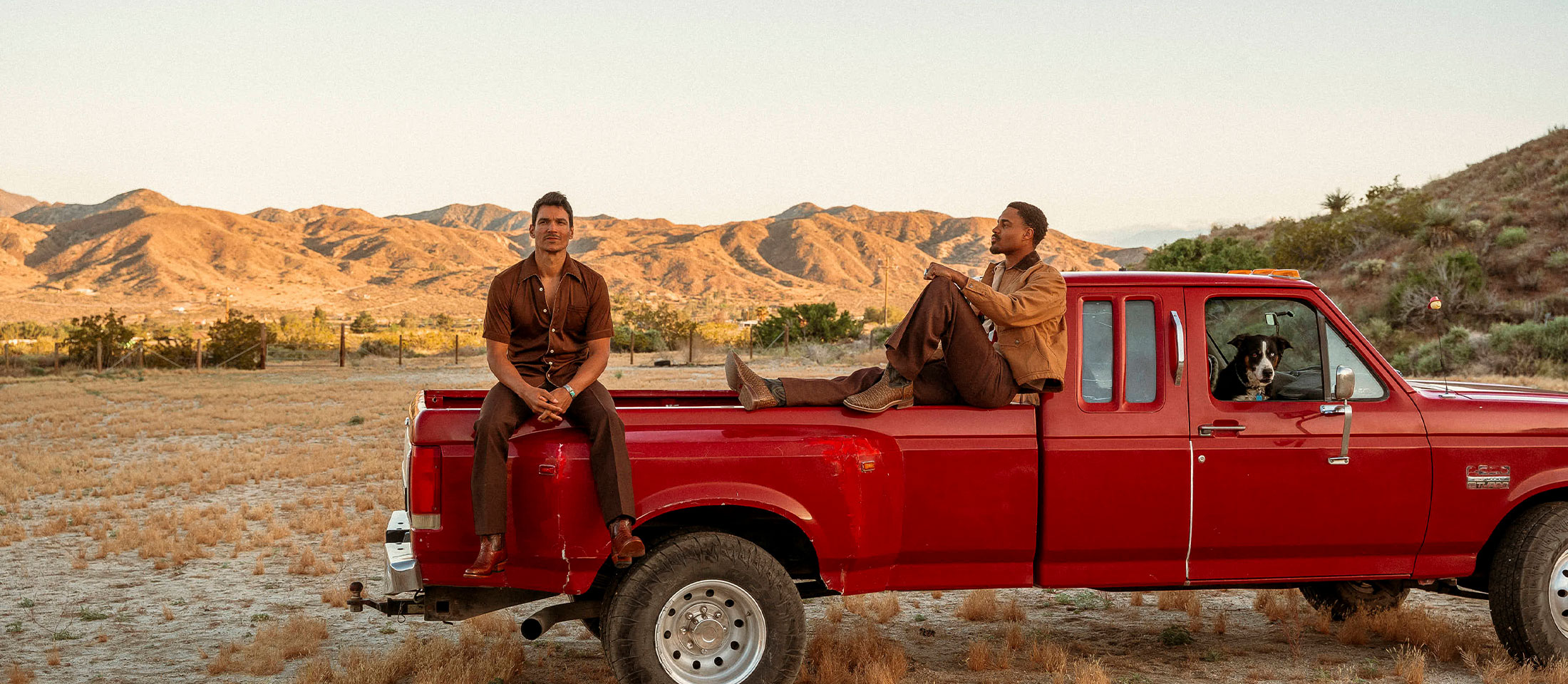 Two men sitting in a red truck with a dog wearing Tony Lama boots: Galán 13" brown cowboy boots and 13" brown Nile crocodile Kango boots.